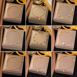 Collection of nine gold titanium steel anklets with floral and heart charms on beige boxes