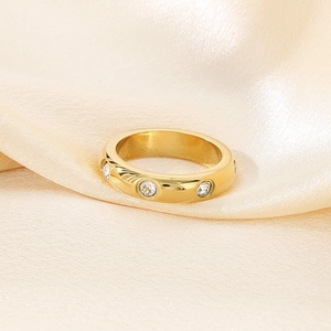 Detail of a polished 18K gold-plated wide band ring with inlaid crystals on silk fabric