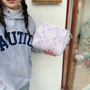 Gros plan d'une trousse de toilette matelassée violette à motifs tenue à la main