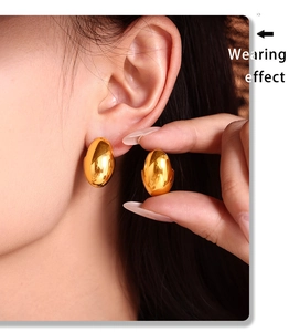 Macro view of gold oval hoop earrings with polished mirror finish on model ear