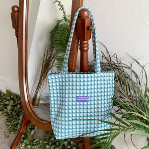Detailed texture of blue and white plaid woven tote bag hanging on a mirror stand