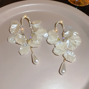 Détail de boucles d'oreilles à fleurs blanches, strass brillants et perles en forme de goutte