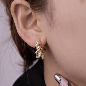 Detail view of twisted croissant style gold earrings on model with polished finish
