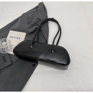 Top view of sleek black underarm bag on white fabric with minimalist props