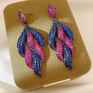 Detailed close-up of leaf-shaped earrings with blue and pink crystals on velvet