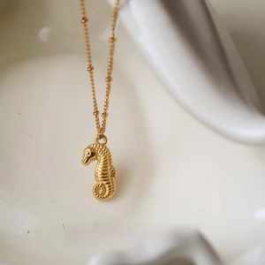 Detailed close-up of golden seahorse pendant with textured surface on a satellite chain