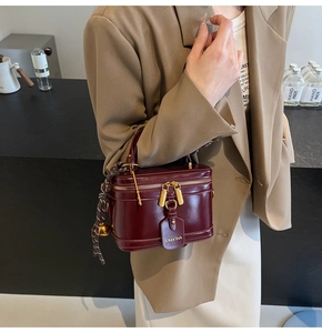 Detail of burgundy patent leather mini box bag with gold zipper held by a model
