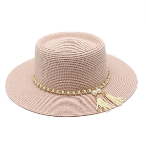 Détail d'un chapeau de paille rose avec chaîne dorée, perles blanches et pompons