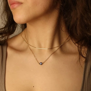 Close-up of double layered gold necklace with blue evil eye pendant on a model