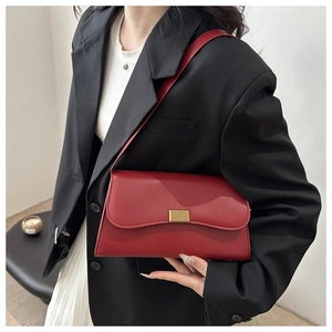 Detail of red leather baguette bag with golden metal buckle worn by model in black suit
