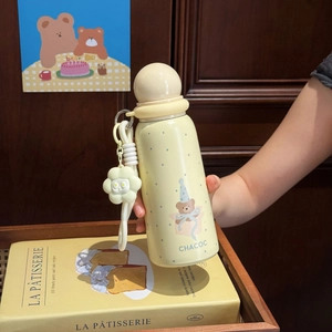 Detail of cream yellow cartoon thermos with bear print, floral pendant, and hand strap
