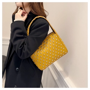 Detailed view of yellow leather tote bag with silver studs on a black blazer