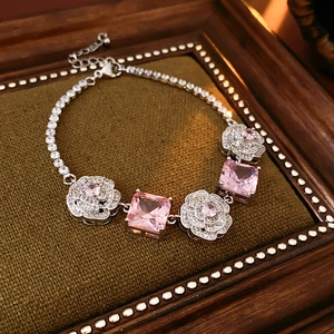 Detail of silver bracelet with pink square gemstones and floral charms on velvet