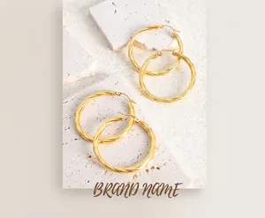 Detail of gold twisted rope hoop earrings resting on a textured white stone surface