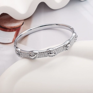 Polished silver metal bangle with teardrop relief and pavé texture on a white surface