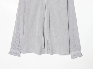 Detail of grey striped shirt featuring ruffle cuffs and white round button closure
