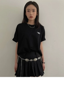 Détail d'une ceinture chaîne en métal vintage sur une mini-jupe plissée noire