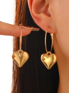 Close-up of shiny gold heart-shaped charm hoop earrings worn on model for fashion look