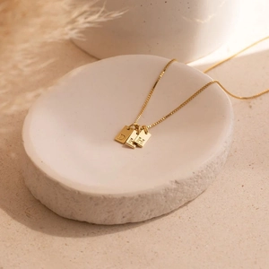 Detail of three rectangular gold letter pendants D, K, H on a box chain necklace