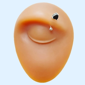 Close-up of eyebrow piercing jewelry with black heart zircon on silicone model eye