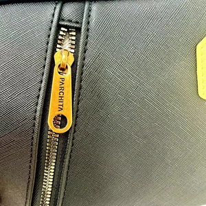 Macro view of gold-tone zipper with PARCHITA engraving on black Saffiano leather bag