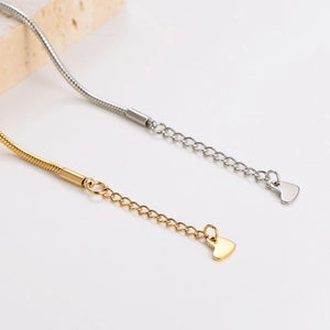 Elegant gold and silver snake chain bracelets with heart charms on marble display