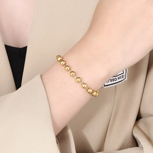 Detailed view of a gold-colored bead chain bracelet worn by a model on a beige blazer