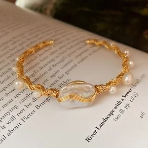 Macro shot of baroque pearl cuff bracelet with gold wire wrapping on vintage paper background