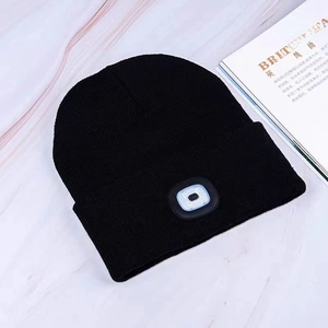 Black knit beanie with integrated LED light on marble background with fashion magazine