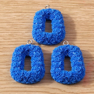 Close-up of blue resin rose relief letter charms with metal loops for DIY jewelry
