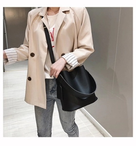Close-up of a black leather bucket bag with a wide strap on a model wearing a beige blazer