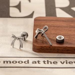 Pair of bow-shaped screw-back studs in polished titanium steel on a rustic wooden table