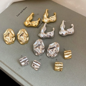 Flat lay of multiple irregular gold and silver textured acrylic earrings on a grey book