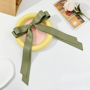 Detailed view of an olive green satin double-layer bow hair clip on a pink ceramic plate