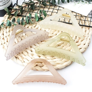 Matte triangle hair claws in cream, khaki, green, and pink on a woven mat