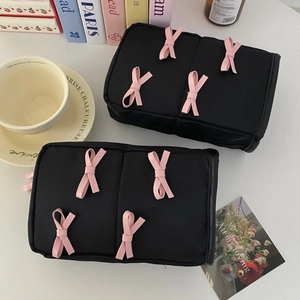 Detail of black fabric makeup bags with pink bows on a clean white desk setup