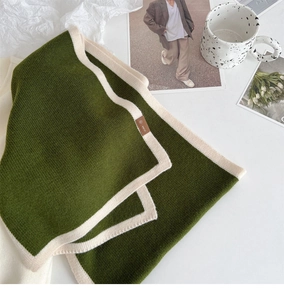 Detailed macro shot of a green knit scarf with beige borders and a leather brand label