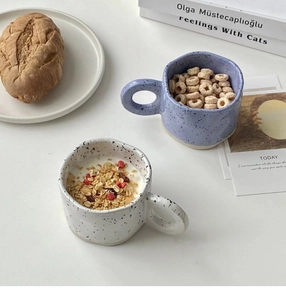Detail view of two irregular splash ink ceramic mugs with cereal on a breakfast table