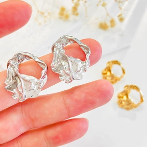Dettaglio di orecchini metallici irregolari in oro e argento tenuti tra le dita