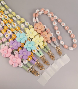 Detailed flat lay of colorful hand-woven cotton phone lanyards with floral charms and gold clips