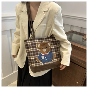 Detail of a brown plaid tote bag with cartoon bear embroidery on a beige coat model