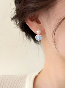 Detail showing elegant pearl and blue petal-shaped crystal earring on a model