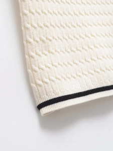 Detailed macro view of cable knit texture and black striped hem on a white polo sweater