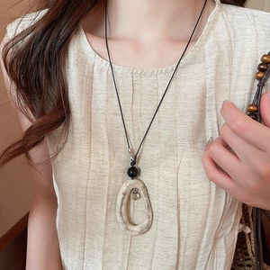 Gros plan du pendentif ovale en acrylique marbré avec perle noire sur collier long