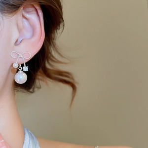 Close-up of a silver bow pearl earring with zircon drop shown on a female model