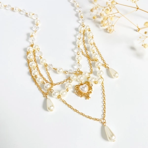 Elegant multi-layer gold chain necklace with white pearls and heart pendant on white background