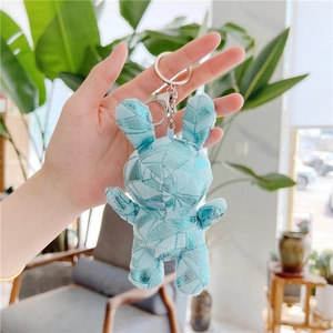 Close-up of light blue plush bunny keychain with metallic geometric prints and silver ring