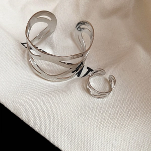 Detail of silver hollow geometric bracelet and matching ring on a beige jewelry pouch
