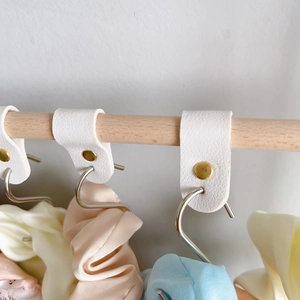 Close-up of white PU leather loops with gold rivets and silver S-hooks for hair accessories