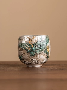 Detailed view of silver ceramic teacup with intricate green and gold dragon motif pattern